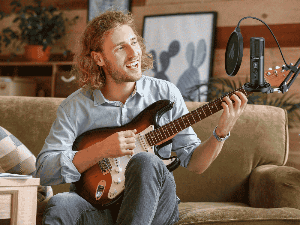 A male musician recording with his condenser microphone and electric guitar