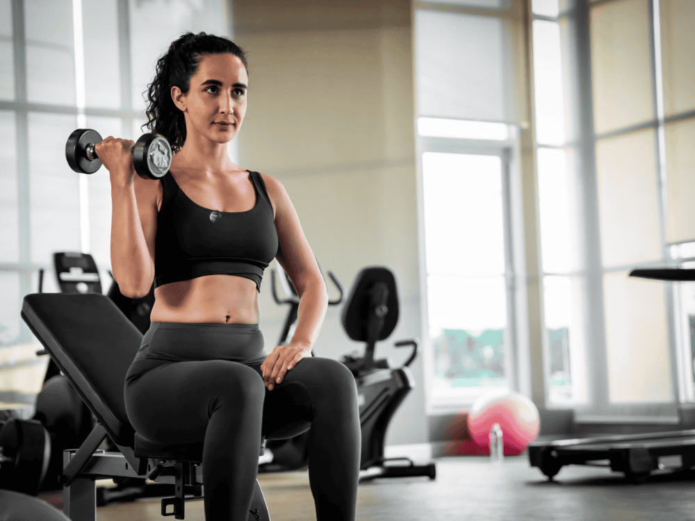 A woman lifting weights and video recording with a wireless microphone